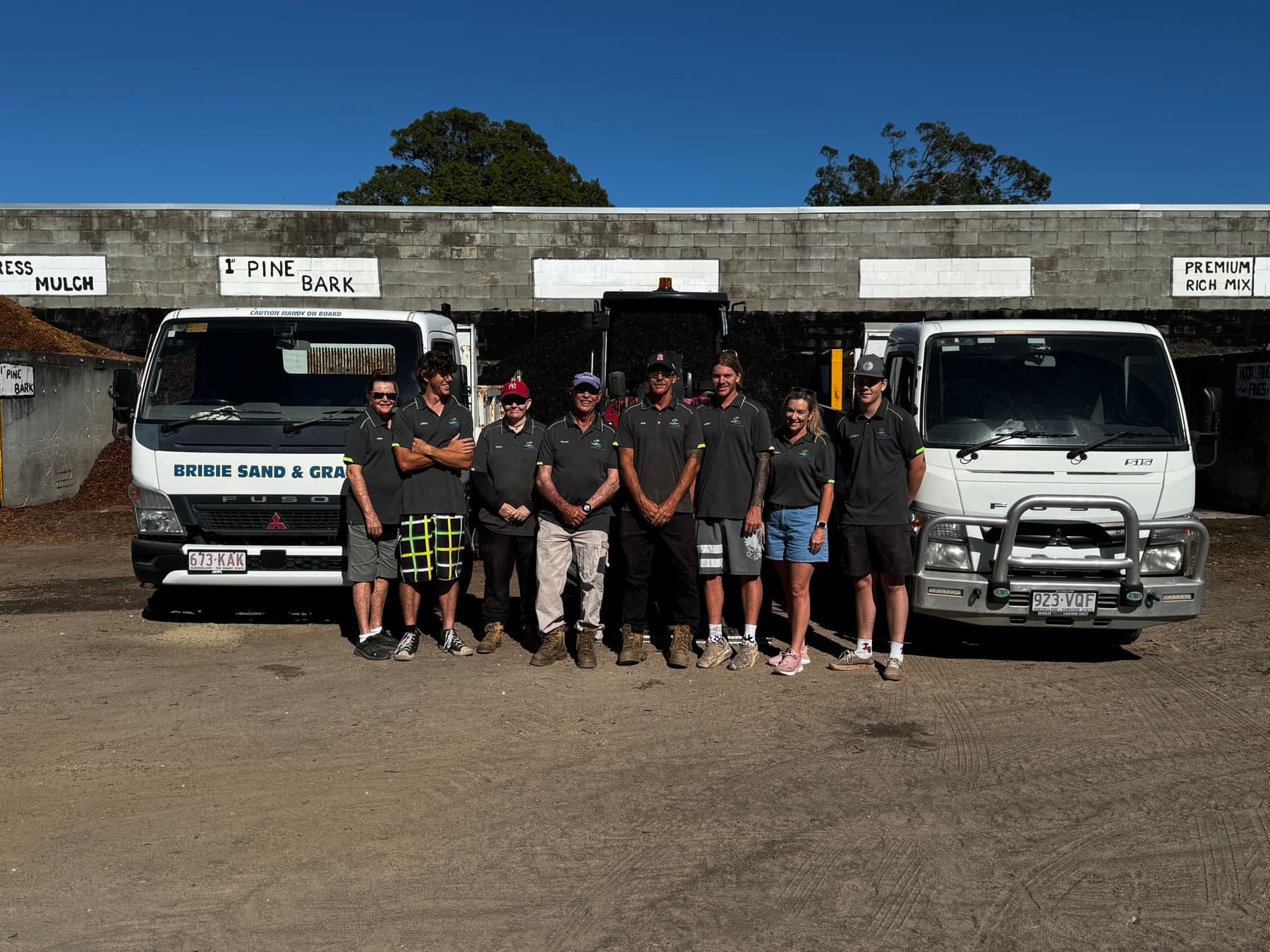 Bribie Sand and Gravel team standing between yard trucks in the supply yard